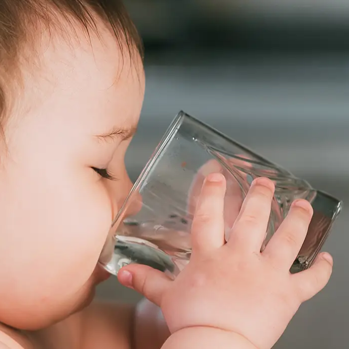 Baby drinking water from clear glass, mess-free mealtime solution for parents