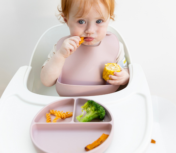Baby eating corn and pasta with mess-free silicone bib and divided plate, easy clean, food-safe design