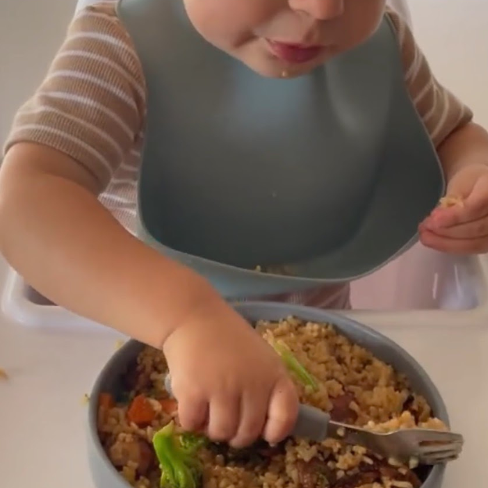 Toddler eating rice and veggies with bib, mess-free mealtime solution