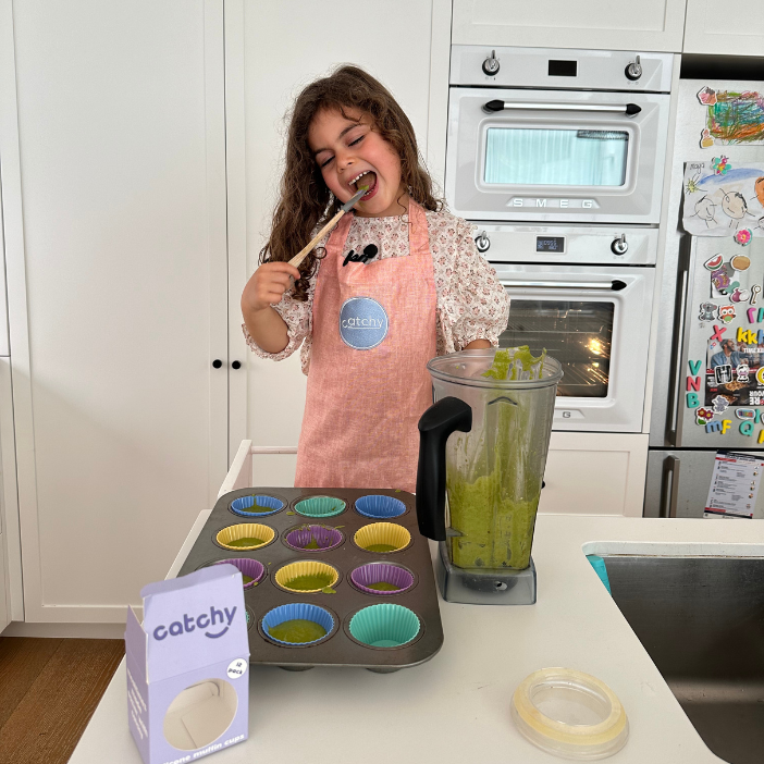 Child baking with colorful silicone muffin cups, blender, and Catchy food catcher apron in modern kitchen