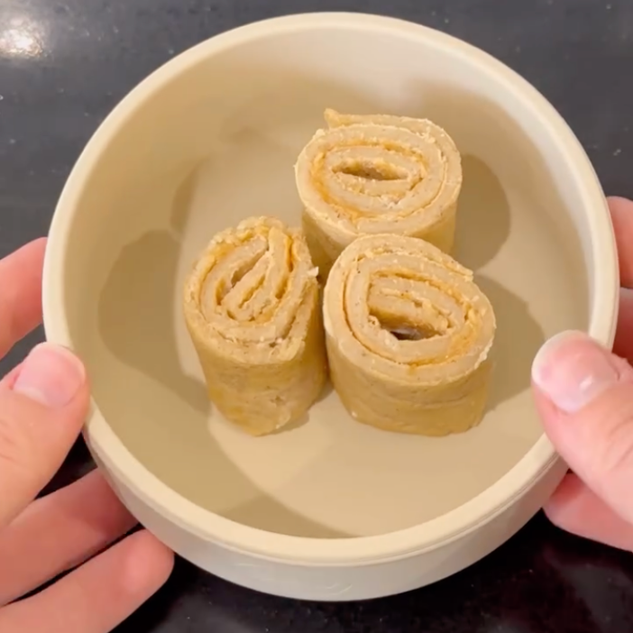 Hands holding a bowl with three rolled-up peanut butter and banana snacks, ideal for mess-free meals.