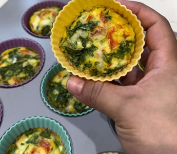 Hand holding yellow silicone egg muffin cup with spinach and tomato, baked in muffin tin