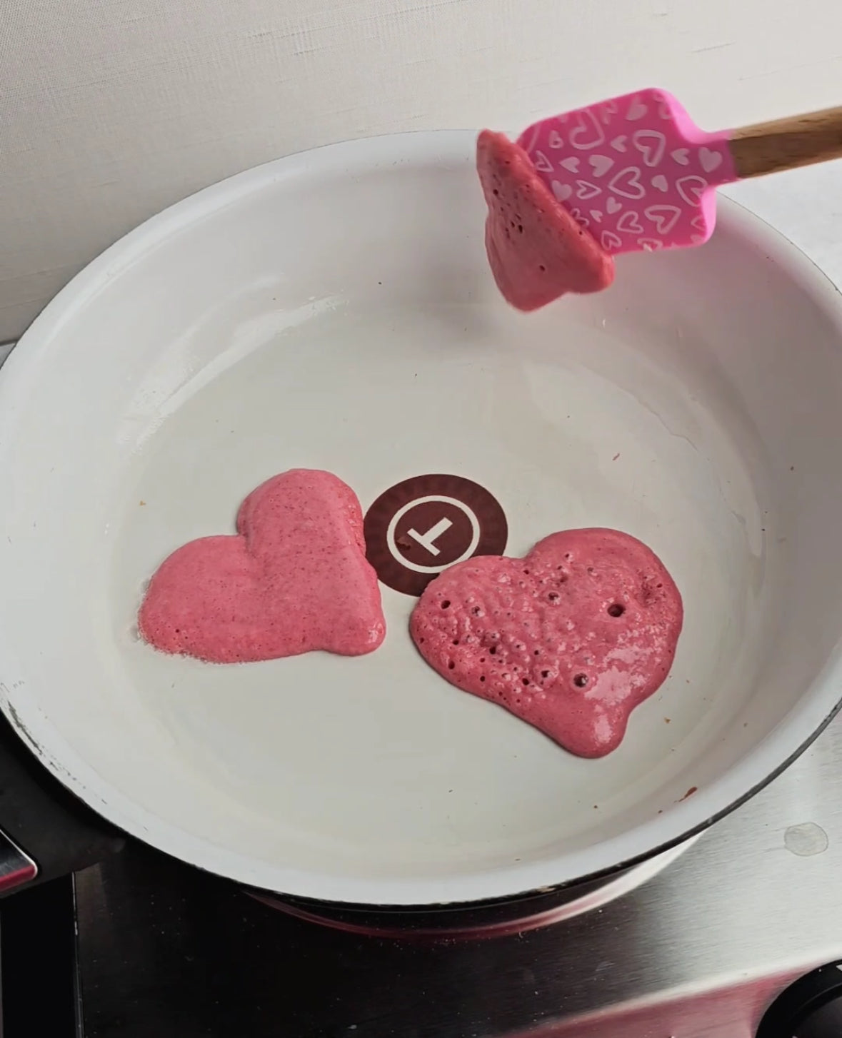 Pink heart-shaped pancakes cooking in white pan with spatula, perfect for mess-free family meals