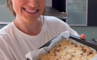 Woman smiling while holding a baking tray with chocolate chip oat bars, ready to bake.