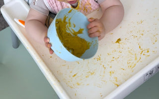 Baby eating messy puree in high chair with food-safe catch mat, easy wipe clean, protects floors