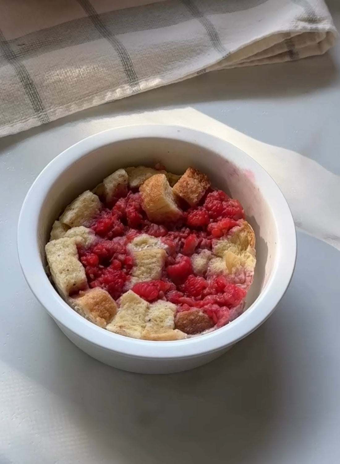 Raspberry bread pudding in white ramekin, fresh baked dessert with juicy berries and golden cubes