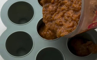 Pouring baby food puree into silicone storage cups for easy meal prep and freezing.